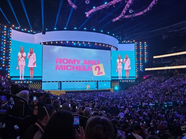 Two women appear on stage in front of a screen with the words 