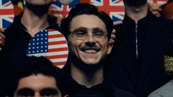 actor Timoth&eacute;e Chalamet smiles and holds a ping pong paddle in the film Marty Supreme